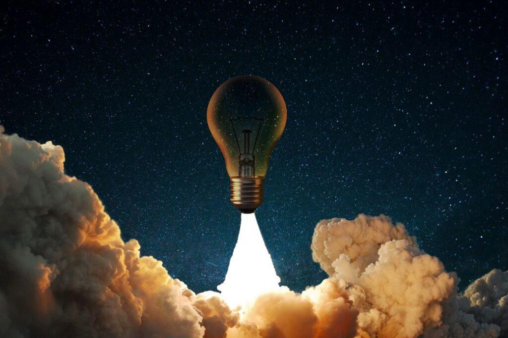 Eine Glühbirne hebt wie eine Rakete in den Sternenhimmel ab, symbolisch für eine zündende Geschäftsidee oder den Start eines Startups